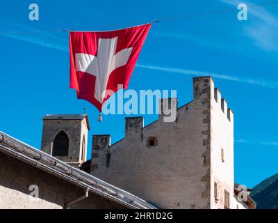 Mustair, Suisse - 28 septembre 2021 : drapeau national suisse au-dessus des murs médiévaux du village suisse de Mustair, dans le canton de Graubunden. Banque D'Images