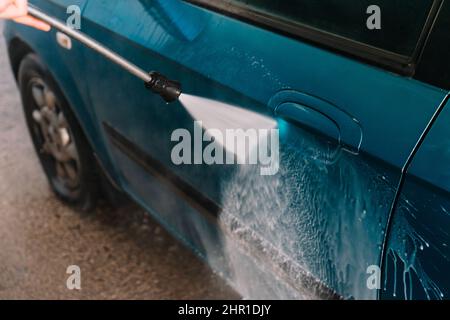 Détail d'un tuyau de lavage de voiture en fonctionnement, sur une voiture bleue. Banque D'Images