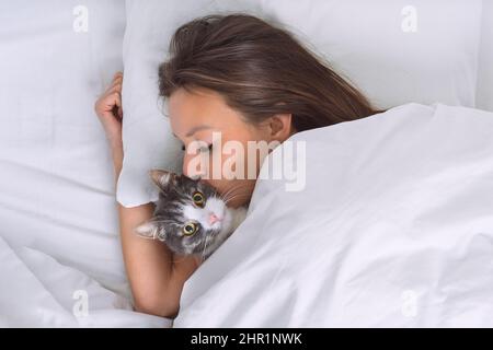 Belle femme couchée dans le lit et embrassant son joli chat. L'amour pour les chats ou les personnes et les animaux de compagnie Banque D'Images