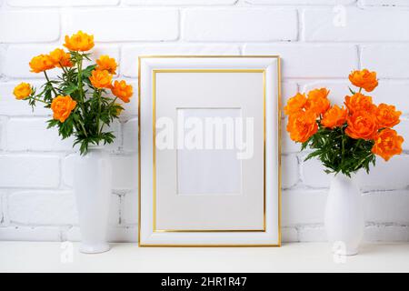 Maquette de cadre blanc à la décoration dorée avec deux vase et globeflowers près du mur en briques peintes. Maquette de cadre vide pour la maquette de présentation. Modèle frami Banque D'Images