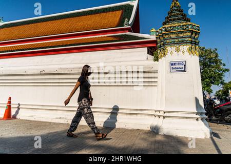 Bangkok, Thaïlande. 25th févr. 2022. Une femme marche jusqu'à l'entrée de Wat Pho à Bangkok. La vie quotidienne autour de Bangkok alors que la Thaïlande se prépare à assouplir les exigences du programme « Test and Go », son programme d'entrée sans quarantaine pour les touristes internationaux pleinement vaccinés. L'assouplissement des exigences d'entrée vient du fait que le pays connaît une augmentation des infections à COVID-19, avec une moyenne de plus de 20 000 cas signalés par jour. Crédit : SOPA Images Limited/Alamy Live News Banque D'Images