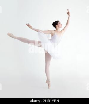 Parfait arabesque. Jeune ballerine élégante dansant à pointe sur fond blanc. Banque D'Images