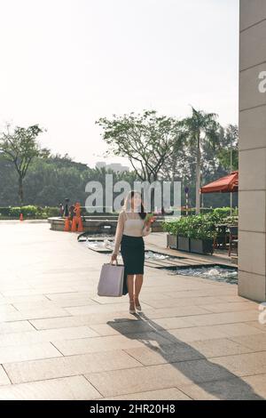 Bonne femme de mode-monger avec des sacs de shopping marchant dans la rue Banque D'Images