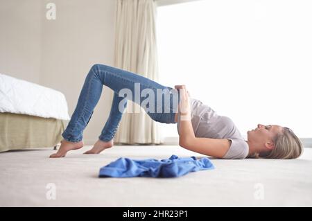 C'est tout simplement trop petit. Une jeune femme qui se bat pour tirer sur son Jean. Banque D'Images