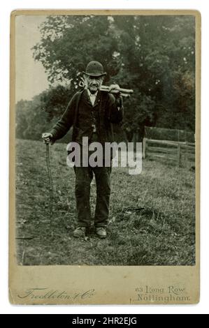 Original et rare carte d'armoire victorienne d'un ouvrier agricole plus âgé de classe ouvrière pauvre, portant sa combinaison de travail patchée, un chapeau de bowling typique des ouvriers agricoles de l'époque, transportant des outils agricoles, peut-être des houes, des râteaux ou des billons. Son apparence de vie dure - il est de l'âge du pensionné. Photo de Freckleton & Co., 63 long Row, Nottingham, Royaume-Uni vers 1890. Banque D'Images