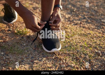 Gros plan de Black jeune adulte athlète masculin nouant ses lacets sur sa chaussure de sport noire. Banque D'Images