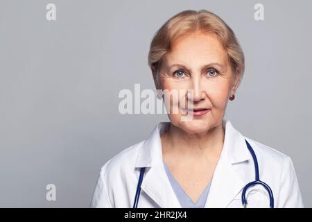 Moyenne adge médecin femme portant l'uniforme médical sur fond gris souriant gai, mûr visage gros plan Banque D'Images