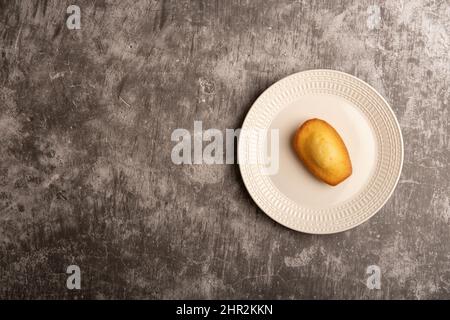 Gâteau Madeleine sur une plaque blanche contre un fond gris texturé béton plat. Banque D'Images