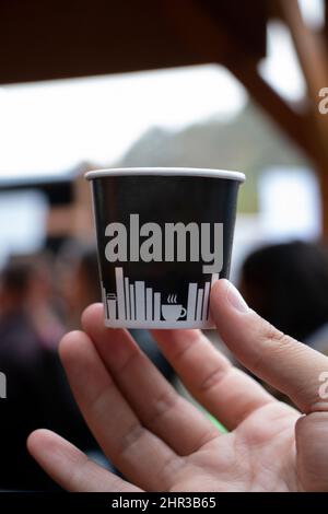 un homme tenant sa main une tasse en plastique blanc. Il montre la tasse sans marque dans sa main. L'arrière-plan est flou. Banque D'Images