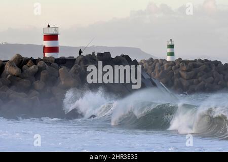 Pêcheurs sur la jetée en pierre avec phares, grandes vagues s'écrasant sur la côte de Nazaré au Portugal. Banque D'Images