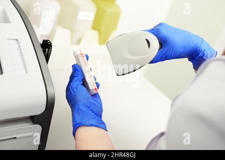 un technicien médical portant des gants en caoutchouc bleu lit le code du tube à essai dans un laboratoire biochimique moderne. Banque D'Images