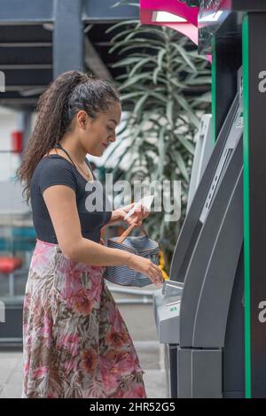 Coup de feu vertical d'une jeune femme hispanique qui retire de l'argent d'un guichet automatique Banque D'Images