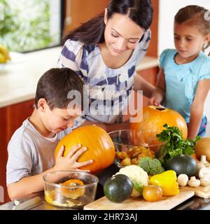 Je pense que c'est prêt. Prise de vue d'une mère qui aide ses enfants à sculpter des citrouilles pour halloween. Banque D'Images