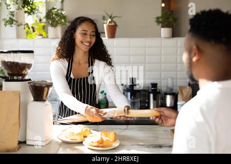 Un barista afro-américain souriant sert un client masculin au comptoir du café Banque D'Images