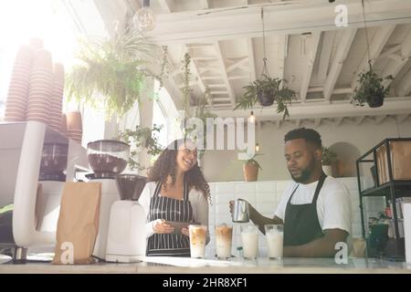 Bonne femme Barista afro-américaine regardant un collègue qui prépare un café glacé au café Banque D'Images