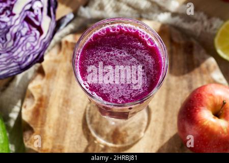 Un verre de jus de chou violet fait maison avec des fruits et des légumes frais en arrière-plan Banque D'Images