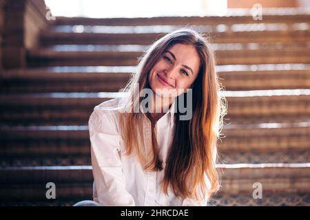 Portrait d'une jeune femme gentille et chaleureuse assise sur les escaliers. Banque D'Images