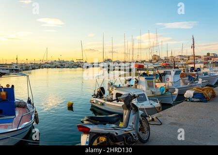 Des bateaux de pêche colorés rouge, blanc et bleu bordent le port de l'île grecque d'Aegina, Grèce, au coucher du soleil. Banque D'Images