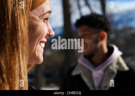 Vue en profil du visage d'une femme souriante avec un homme souriant non focalisé en arrière-plan Banque D'Images