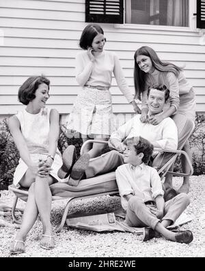 1960S PÈRE SOURIANT ASSIS DANS UNE CHAISE LONGUE EXTÉRIEURE ENTOURÉE DE SA FEMME DEUX FILLES ADOLESCENTES ET SON FILS ASSIS SUR LUI JOURNAUX - J13201 HAR001 HARS VÊTEMENTS NOSTALGIQUE PAIRE SUBURBAIN VIEUX TEMPS NOSTALGIE VIEILLE MODE JEUNE STYLE COMMUNICATION FORTS FILS HEUREUX FAMILLES JOIE VIE SATISFACTION CHAISE CINQ FEMMES MAISONS MARIÉES 5 ÉPOUX ÉPOUX SANTÉ MAISON VIE COPIE ESPACE FEMMES PLEINE LONGUEUR DEMI-LONGUEUR FEMMES SALON FILLES PERSONNES RÉSIDENTIEL SOINS HOMMES JOURNAUX ADOLESCENTS FILLES BÂTIMENTS ÂGE MOYEN PARTENAIRE B&W HOMME D'ÂGE MOYEN BONHEUR JOYEUX SES LOISIRS ET L'EXCITATION EST ENTOURÉE Banque D'Images