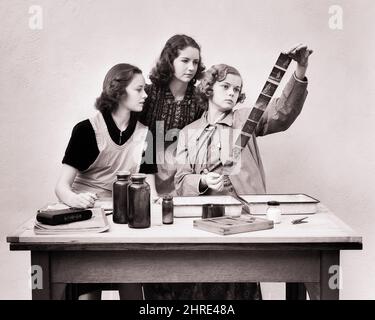 1930S 1940S TROIS JEUNES FEMMES TECHNICIENS DE LABORATOIRE DE PHOTOGRAPHIE INSPECTANT UN ROULEAU DE FILM NÉGATIF NOIR ET BLANC DÉVELOPPÉ POUR APPAREIL PHOTO - J8221 HAR001 HARS INFORMATION CHIMIE DÉTENTE STYLE DE VIE CÉLÉBRATION FEMMES EMPLOIS ESPACE DE COPIE DEMI-LONGUEUR FEMMES PERSONNES ADOLESCENTES DIVERTISSEMENT FILLE FRÈRES ET SŒURS CONFIANCE SŒURS TABLIERS B&W OBJECTIFS SUCCÈS TRAITEMENT COMPÉTENCE ACTIVITÉ DIVERTISSEMENT PROFESSION PHOTOGRAPHES COMPÉTENCES DÉCOUVERTE HOBBY UNIVERSITÉS INTÉRÊT EXAMINER EXCITATION HOBBIES CONNAISSANCES PROGRÈS LOISIRS PASSE-TEMPS FIERTÉ PLAISIR UN EMPLOI OCCUPATIONS FRÈRE ENSEIGNEMENT SUPÉRIEUR CONCEPTUEL INSPECTION NÉGATIVE Banque D'Images