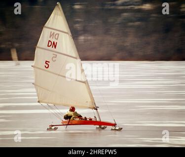 1970S MARIN ANONYME PORTANT UN CASQUE ROUGE PILOTANT UN BATEAU À GLACE OU UN YACHT À GLACE QUI S'EXÉCUTE AU-DESSUS DE LA GLACE SUR DES LAMES MÉTALLIQUES - KW4697 PHT001 HARS À L'ANCIENNE Banque D'Images