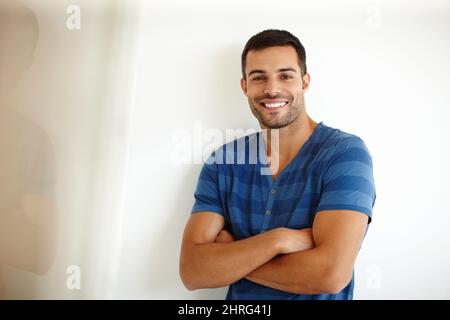 Rempli de positivité. Un beau jeune homme souriant debout avec ses bras pliés. Banque D'Images