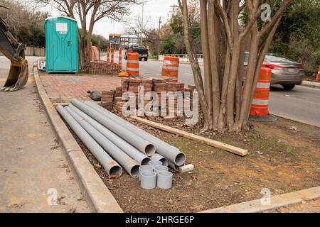 Chantier de construction sur la rue de la ville avec matériaux, toilettes portables, troncs d'arbres et circulation à proximité. Banque D'Images