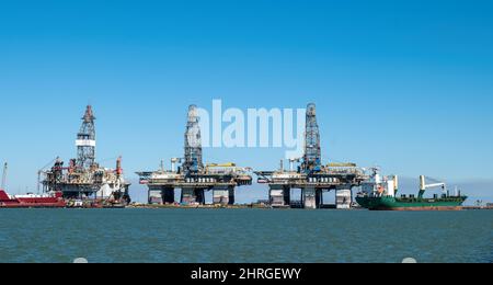 Un navire navigue par trois plates-formes de plates-formes de forage pétrolier offshore dans un quai sec le long du canal d'expédition à Port Aransas, Texas. Banque D'Images