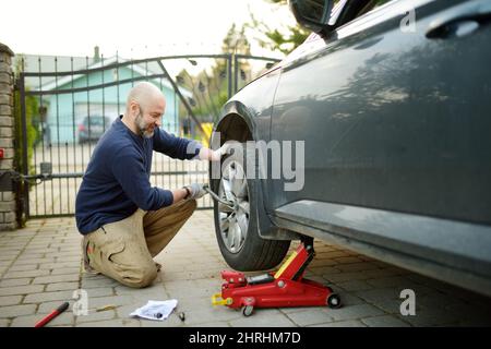 Jeune homme changeant le pneu crevé sur sa voiture. Desserrer les écrous à l'aide d'une clé pour écrous de roue avant de lever le véhicule. Banque D'Images