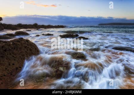 Rochers sur la plage de Curl Curl sur la côte australienne de la côte nord de Sydney au lever du soleil. Banque D'Images