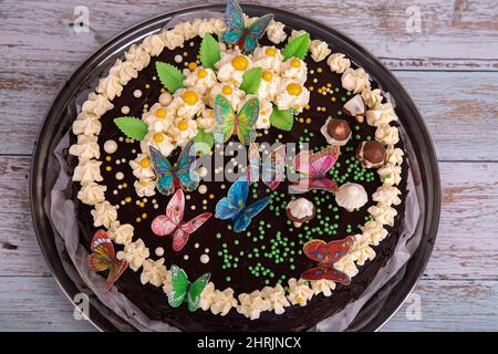 Gâteau au chocolat à la crème blanche, papillons colorés et champignons au chocolat sur fond de bois Banque D'Images