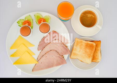 Service de petit déjeuner avec œufs durs, fromage, jambon, tranches de légumes, toasts, café et jus Banque D'Images