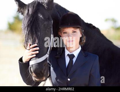 Cheval et cavalier partagent un lien fort Portrait d'une jeune femme pilote qui lui fait face à ses chevaux et qui sourit fièrement à l'appareil photo. Banque D'Images