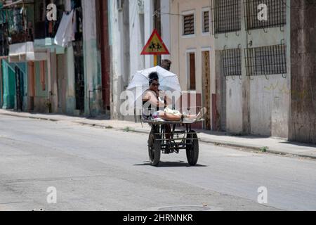 Une femme se déplace à l'arrière d'un vélo le long d'une rue à la Havane, Cuba comme un homme la conduit à travers un quartier. Banque D'Images