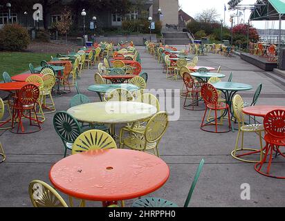 Chaises et tables de patio colorées avec gouttes d'eau sur la surface alignée devant un bâtiment Banque D'Images