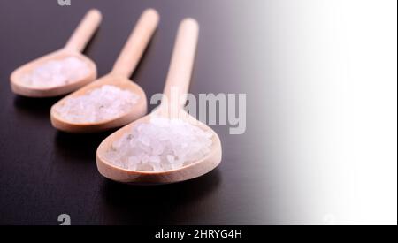 Bath salt in three wooden spoons on a dark polished desk in backlight Banque D'Images