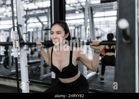 Concept d'exercice la femme en noir tenues de sport portant la machine de poids en la portant sur ses épaules et en essayant de la soulever. Banque D'Images