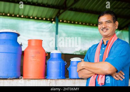 joyeux journal fermier souriant devant des récipients de lait à la maison de ferme avec des bras croisés en regardant la caméra - concpet de l'agriculture laitière réussie et Banque D'Images