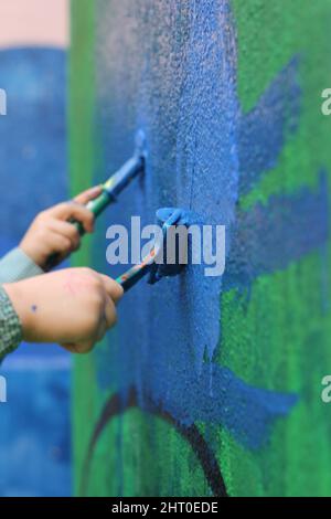 détail des mains des petits enfants avec un pinceau pour peindre un mur Banque D'Images