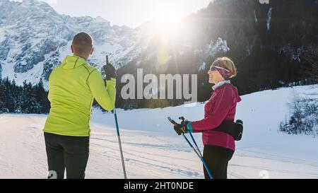 Couple d'âge mûr, skieurs de fond, debout sur une piste de ski et regardant les incroyables sommets des montagnes enneigées. Un homme pointant vers la chaîne de montagnes. Banque D'Images