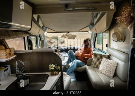 Homme de voyage adulte s'asseoir à l'intérieur moderne confortable mobile maison camping-car van regardant la nature à l'extérieur. Voyagez et vanlife style de vie pour les personnes libres alternatives Banque D'Images