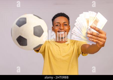 Sport misez excitation, joueur et style de vie de famille concept. Un jeune gars afro-américain enthousiaste qui apprécie leur victoire, se tenant avec le ballon de football et beaucoup Banque D'Images