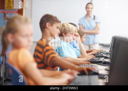 Garder un œil sur sa classe. Un groupe de jeunes enfants travaillant dur en classe informatique. Banque D'Images