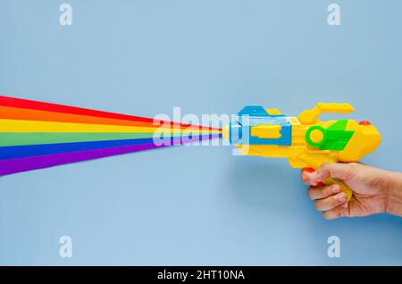 Main tenant le pistolet arrosoir pulvérisé avec du papier de découpe coloré pour la célébration du festival Songkran sur fond bleu. Concept de vacances minimal. Banque D'Images
