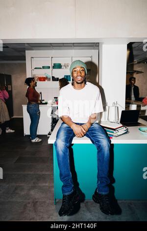 Portrait d'un jeune homme assis sur une table de salle à manger dans la cuisine du dortoir d'université Banque D'Images