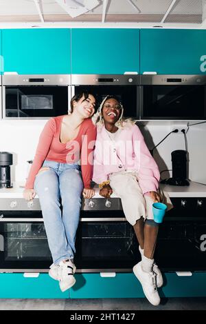 Jeunes femmes heureuses assis sur le comptoir de cuisine dans le dortoir d'université Banque D'Images