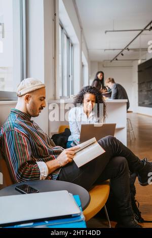 Homme lisant un livre alors qu'une femme utilise un ordinateur portable à l'université Banque D'Images