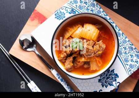 Cuisine asiatique concept bœuf épicé et soupe de Kimchi ou ragoût Kimchi jjigae dans un bol en céramique noire sur carton en bois avec espace pour les copies Banque D'Images