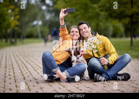 jeune couple caucasien prenant le selfie avec un chien assis sur un chemin dans le parc Banque D'Images